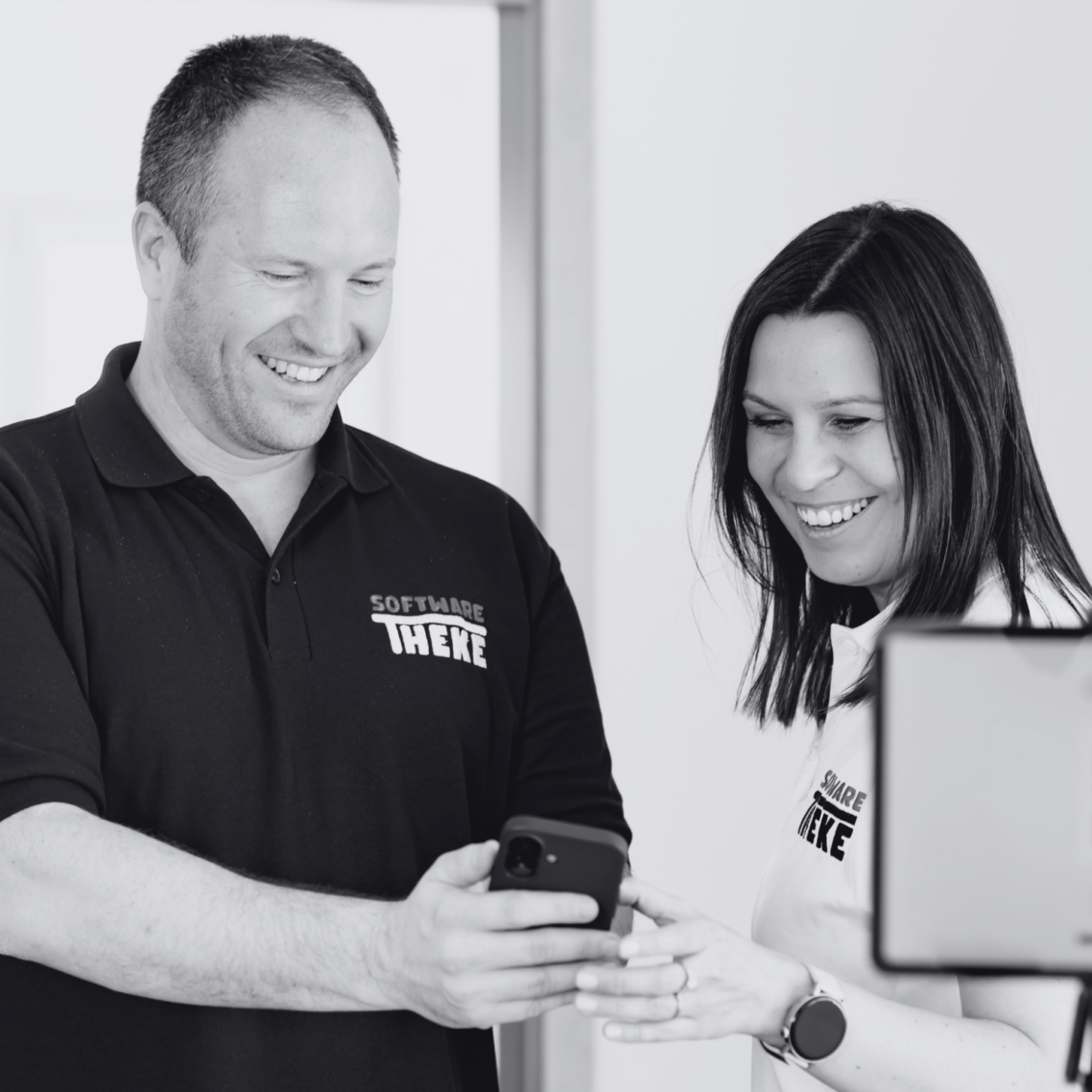 Kontaktieren Sie uns Zwei Personen lächeln, während sie gemeinsam auf ein Smartphone schauen.